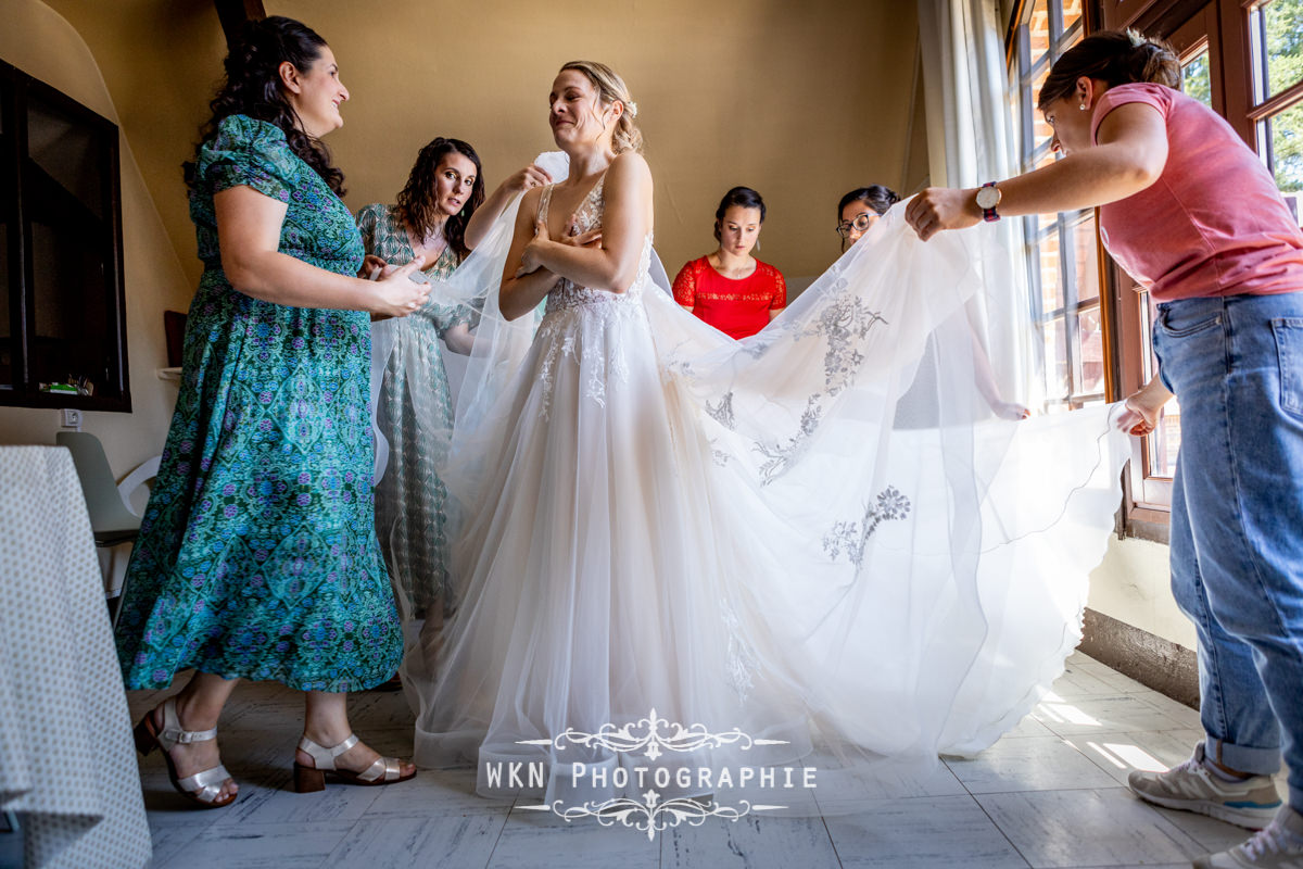 Claire, habillée de sa robe de mariée, entourée de ses proches, émue et prête pour la cérémonie.